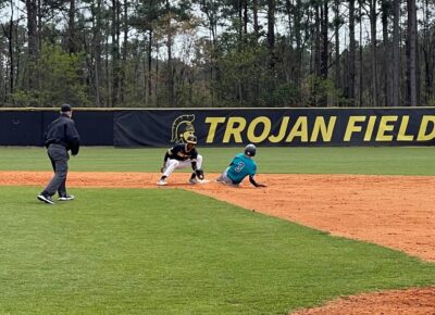 Teammates wait at home plate for a runner to score