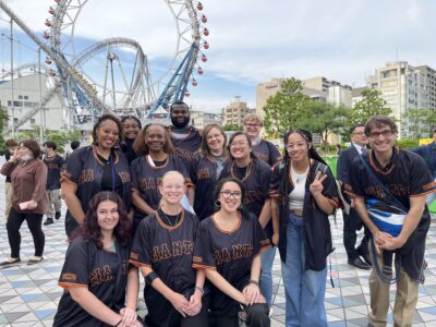 A group of people wearing baseball jerseys stands in front of a roller coaster