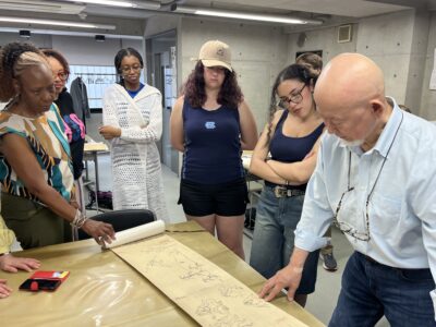 a group of people stand around a table looking at a scroll of Japanese brush painting art.