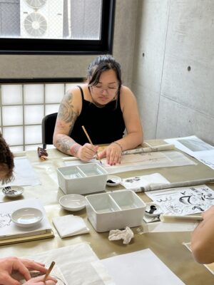 A woman sitting at a table practices Japanese brush painting.