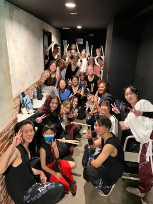 A group of people pose in a hallway. Some of them hold drumsticks.