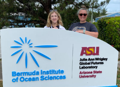 Two women stand behind a sign for the Bermuda Institute of Ocean Sciences.