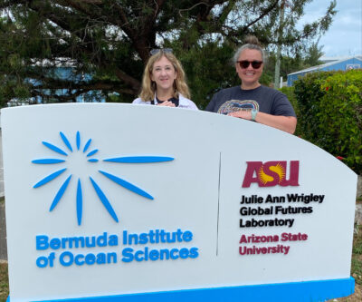 Two women stand behind a sign for the Bermuda Institute of Ocean Sciences.