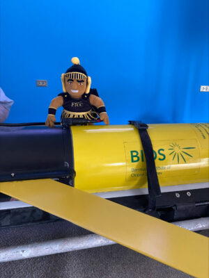 A stuffed toy of FTCC mascot Theo behind a yellow metal cylinder that has the Bermuda Institute of Ocean Sciences logo on it.