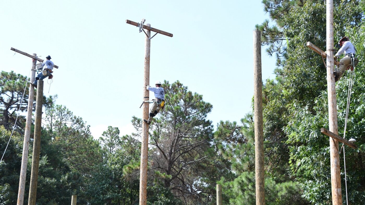 Three men work near the top of electric poles.