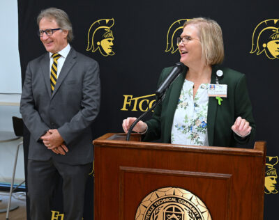 A woman speaks into a microphone at a podium while a man stands beside her.