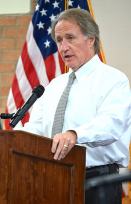 A man in a white dress shirt and tie speaks at a podium.