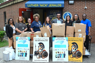 A group of people stand behind carts of cardboard boxes in front of a school entrance.