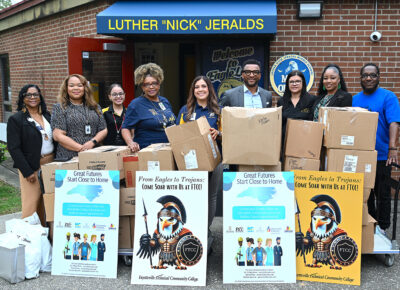 A group of people stand behind carts of cardboard boxes in front of a school entrance.