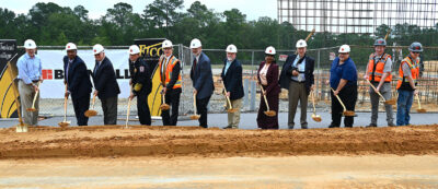 A group of people perform a ceremonial groundbreaking with shovels at a construction site.