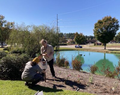 Two people install a sign in a garden near a pond.