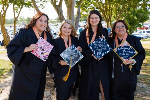 Four graduates show off the tops of their caps, which are decorated, while standing outside the Crown.