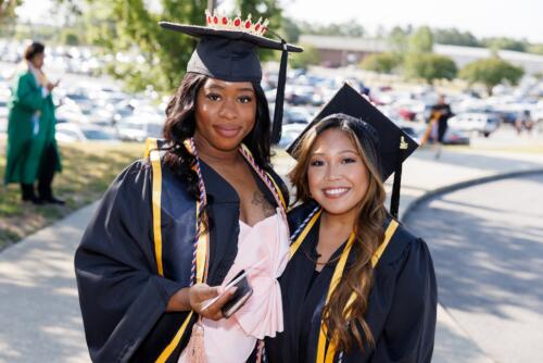 Two graduates in caps and gowns pose for a photo outside of 