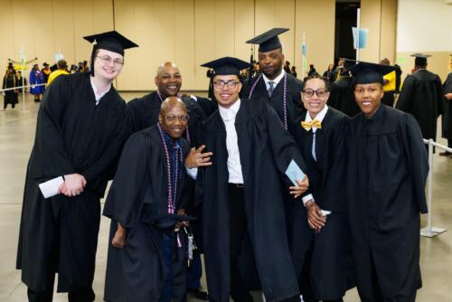 A group of students in caps and gowns pose for a photo in the staging area before graduation.