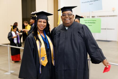 Two graduates, one with a gold stole, pose for a photo in the staging area before graduation.