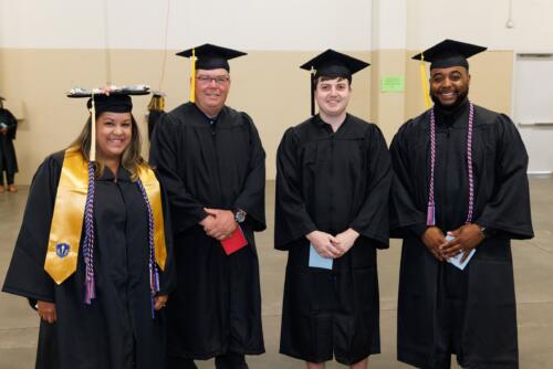 Four graduates, one wearing a gold stole, pose for a photo.