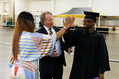 Tammy Thurman high-fives a graduate while Dr. Mark Sorrells looks on.