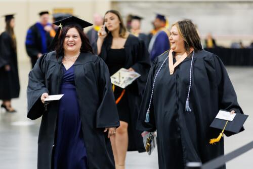 Two graduates talk with smiles on their faces as they walk through the staging area before graduation.