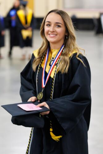 A graduate dressed in gown and stole with cords and a medallion smiles at the camera.