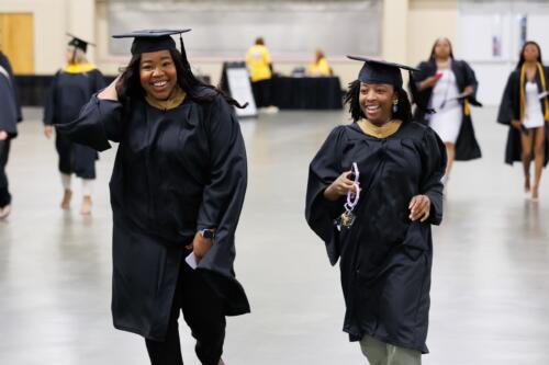 Two graduates laugh as they walk through the staging area.