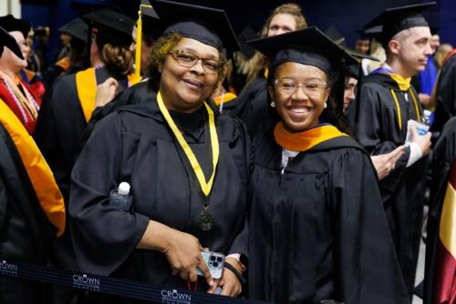 Two faculty members dressed in graduation regalia smile at the camera while standing in the entrance tunnel to the Crown.