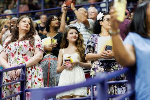 A girl stands in the middle of a group of audience members in the stands.