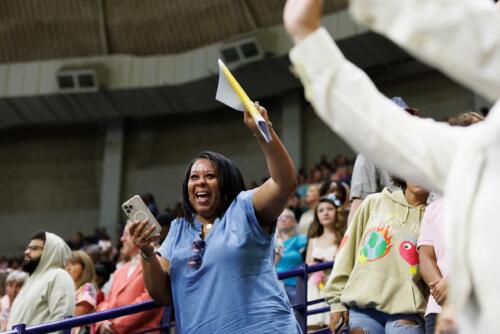 An audience member raises her hand and cheers while standing in the stands.