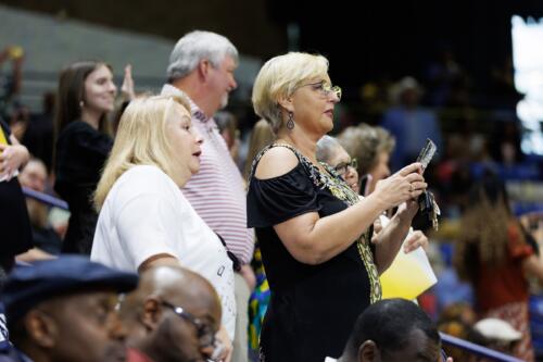 Two women, shown in profile, lean together to talk while standing in the audience.