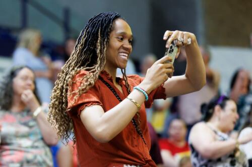 A woman smiles at her phone while she stands in the audience.