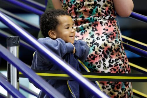 A young child wearing a large sweatshirt smiles as he leans on the railing.