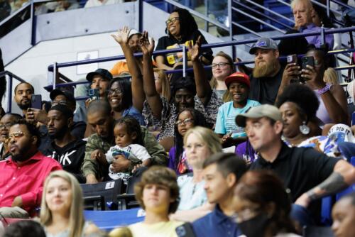 A family in the stands smiles, raises their hands and holds up their phones from their seats.