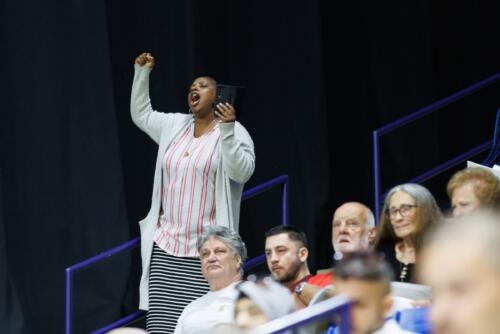 A woman standing cheers from a back row in the audience.