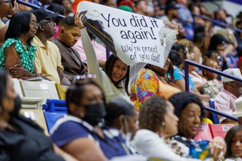 A woman in the stands holds up a sign that says "You did it again! We're proud of you dad!"