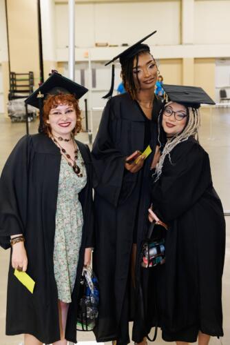 Three graduates pose together for a photo in the staging area.