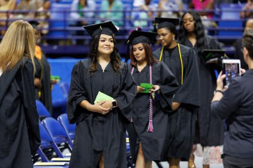 A graduate smiles up at the crowd as she leads a line of graduates into a row of seats.