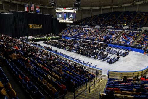 A wide photo of the Crown Coliseum, showing the stage, rows of graduates in seats and the audience seating.