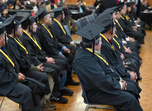 Two rows of graduates dressed in caps and gowns sit at the graduation.