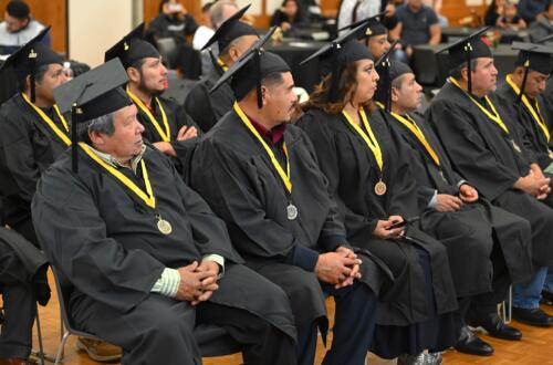 Graduates dressed in caps and gowns sit with their faces turned to show their profiles.