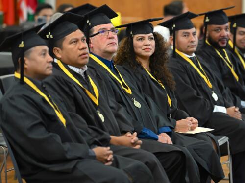 Graduates in caps and gowns sit in a row of seats.