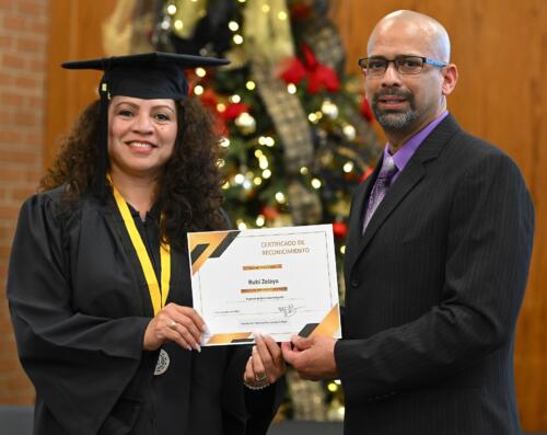 A graduate poses with her certificate while standing next to Miguel Figueroa.