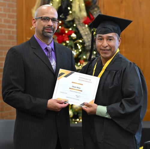 A graduate poses with his certificate while standing next to Miguel Figueroa.