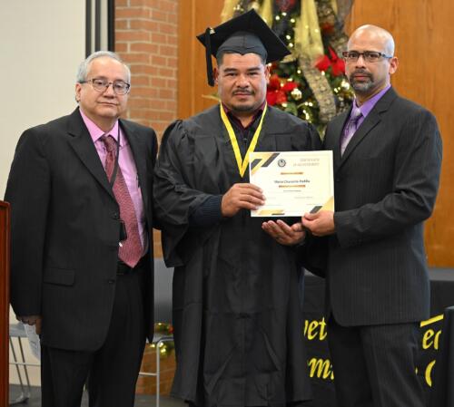 A graduate poses with his certificate while standing next to Miguel Figueroa.