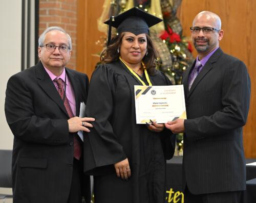 A graduate poses with her certificate while standing next to Miguel Figueroa.