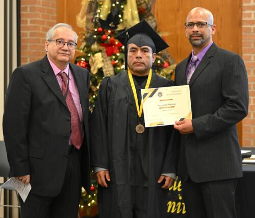 A graduate poses with his certificate while standing next to Miguel Figueroa.