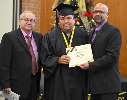 A graduate poses with his certificate while standing next to Miguel Figueroa.