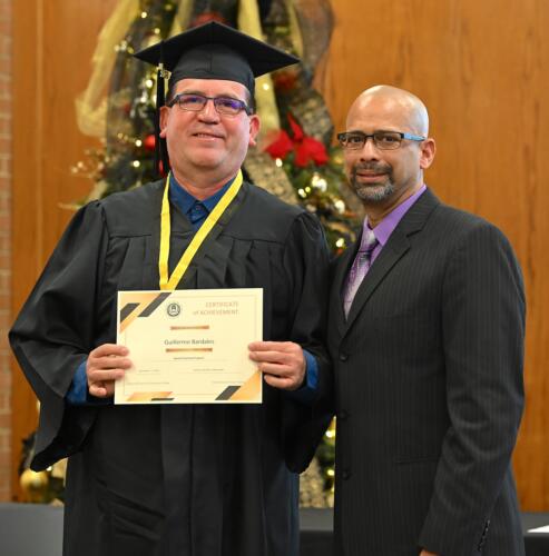 A graduate poses with his certificate while standing next to Miguel Figueroa.