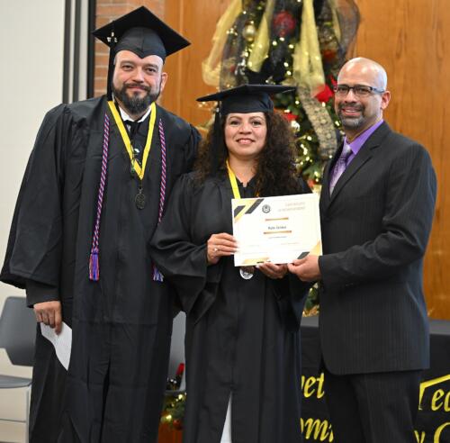 A graduate poses with her certificate while standing next to Miguel Figueroa and her fellow graduate.