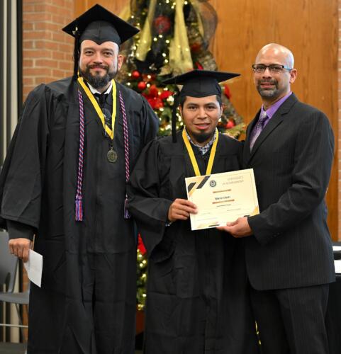 A graduate poses with his certificate while standing next to Miguel Figueroa and his fellow graduate.