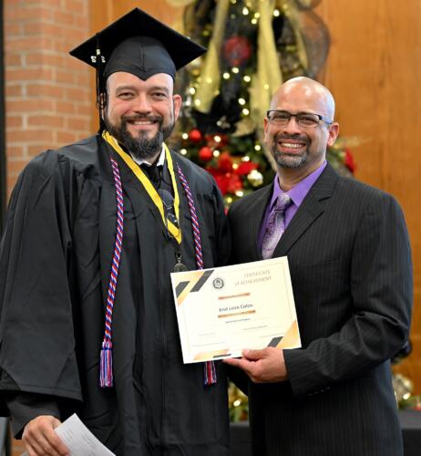 A graduate poses with his certificate while standing next to Miguel Figueroa.