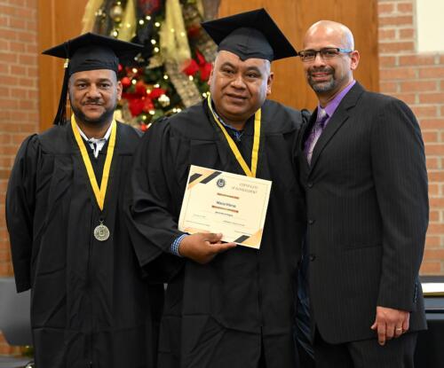 A graduate poses with his certificate while standing next to Miguel Figueroa and his fellow graduate.